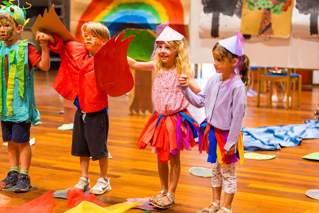 Verkleidete Kinder auf der Bühne halten sich an den Händen – kreative Theateraufführung mit bunten Kostümen und selbstgemalten Kulissen.