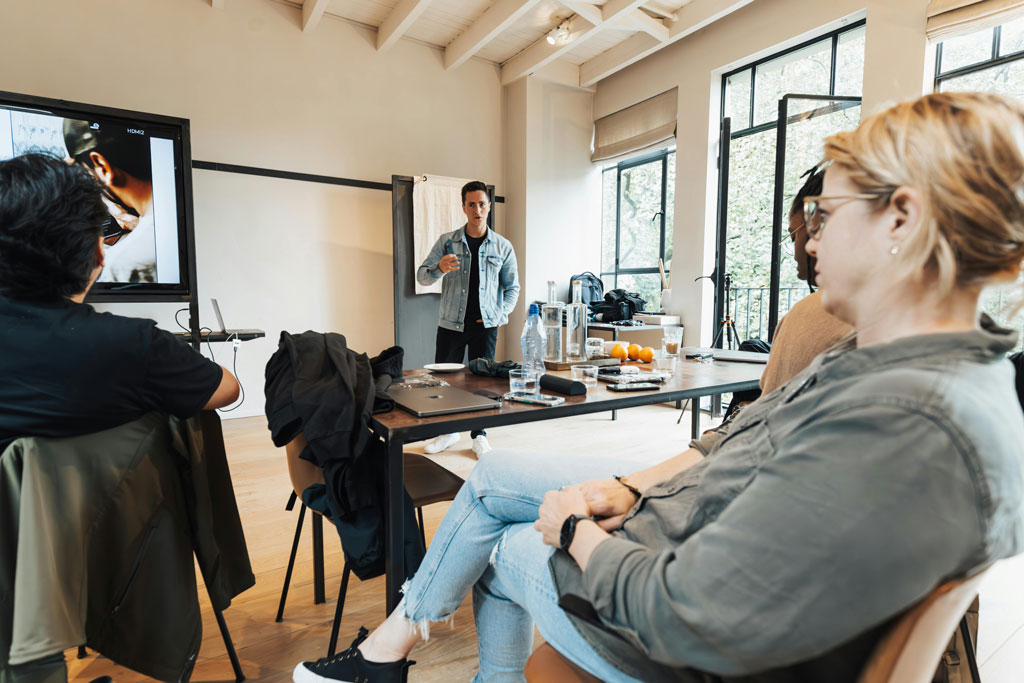 Teilnehmende eines Workshops im Gespräch mit einem Vortragenden – Seminartisch mit Materialien, entspannte Atmosphäre im hellen Raum.